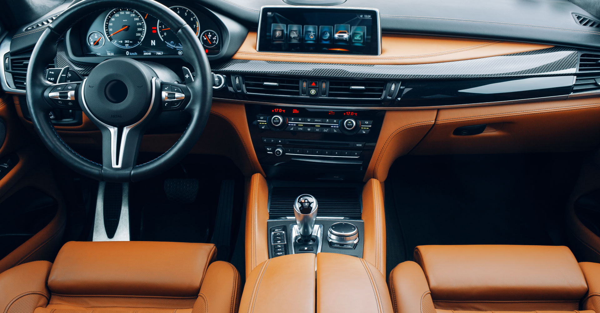 Innenraum eines modernen Fahrzeugs mit lederbezogenem Armaturenbrett und Steuerungselementen.