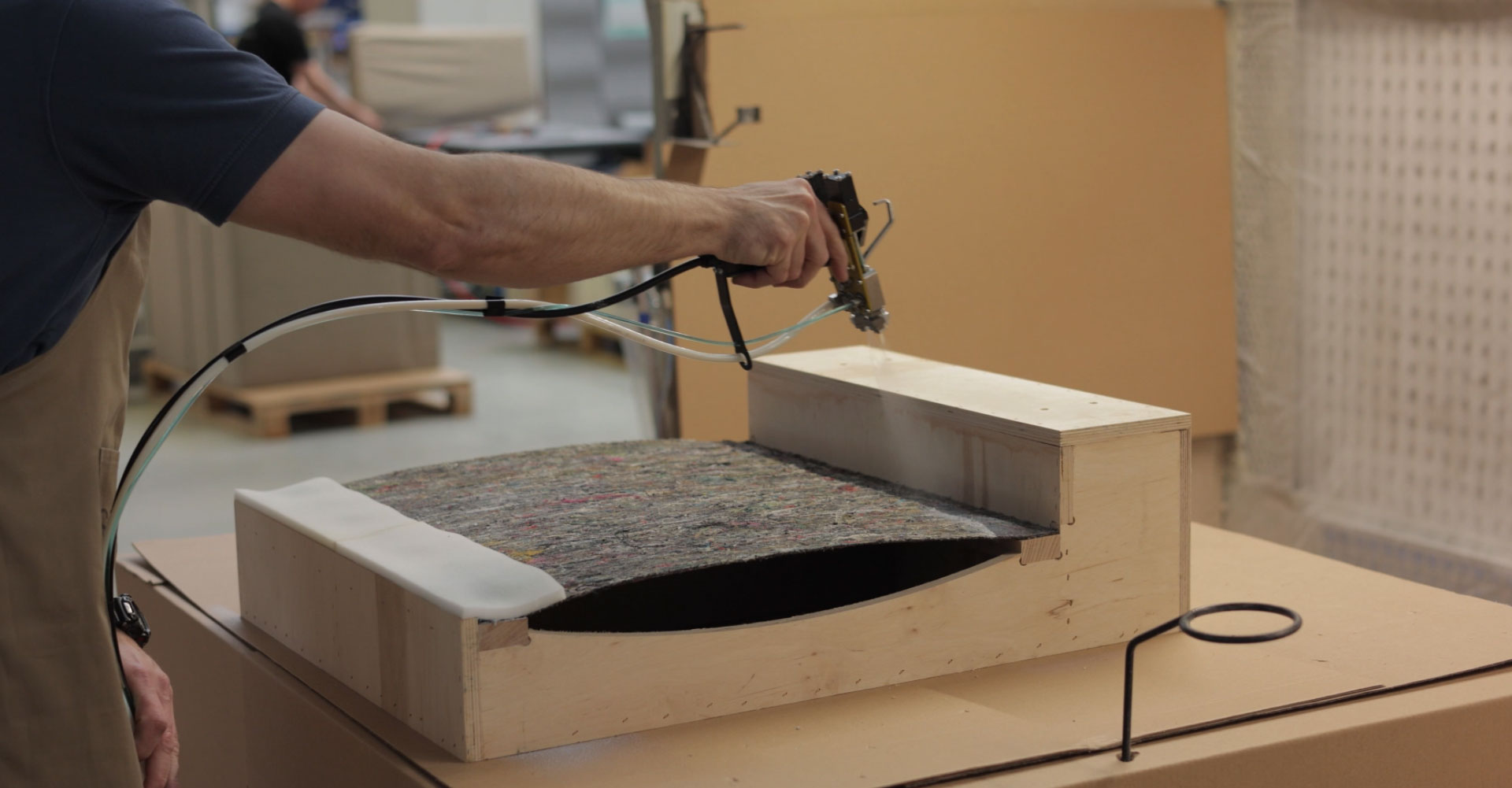 Person, die Sprühkleber auf ein Werkstück aufträgt.