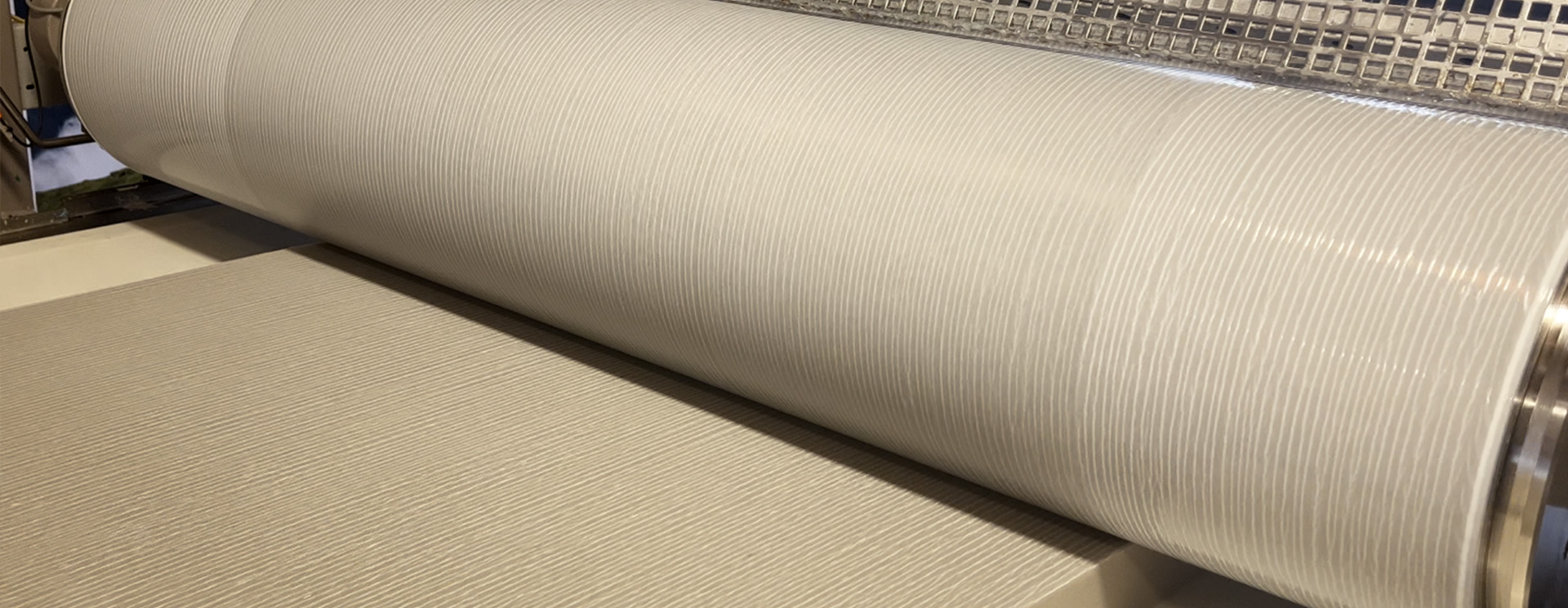 Close-up of a fabric roll being processed by a rolling machine in a manufacturing setting