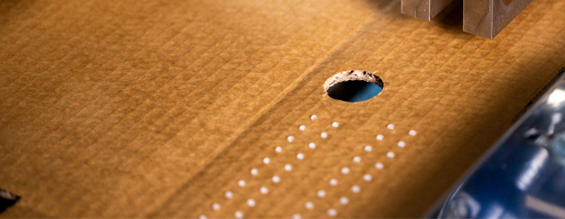 Close-up of cardboard with a round hole and precise dot-and-dab adhesive application.