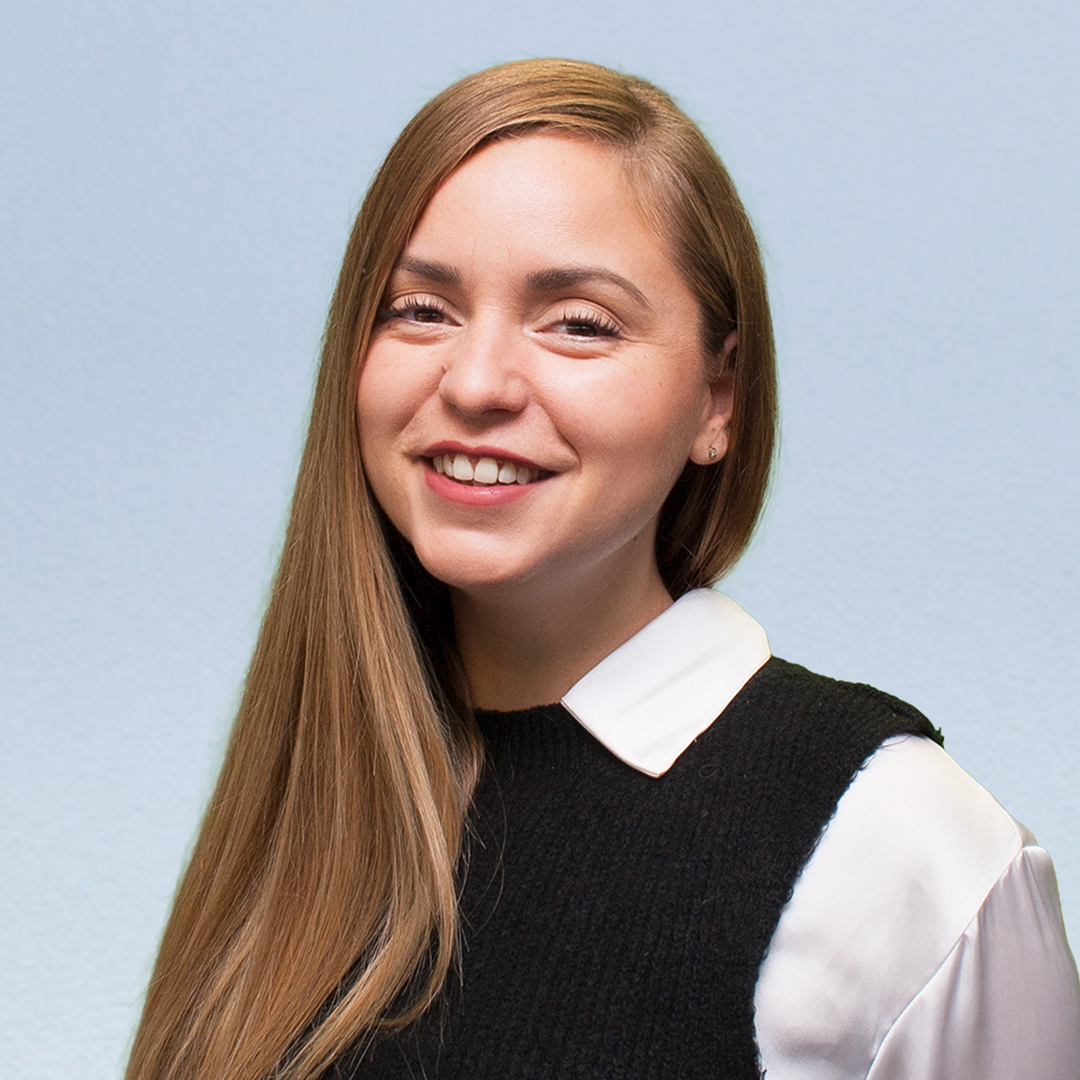 Junge Frau mit langen, glatten, hellbraunen Haaren, lächelnd vor einem hellblauen Hintergrund.