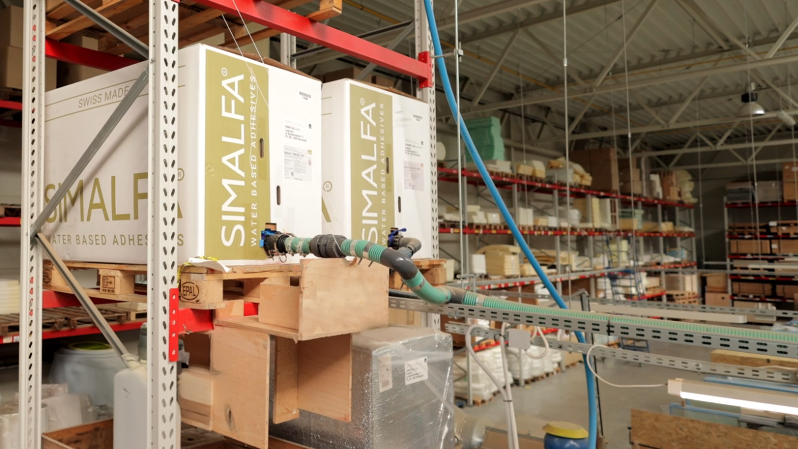 Storage room with large cartons of SIMALFA® water-based adhesives connected to a production plant.