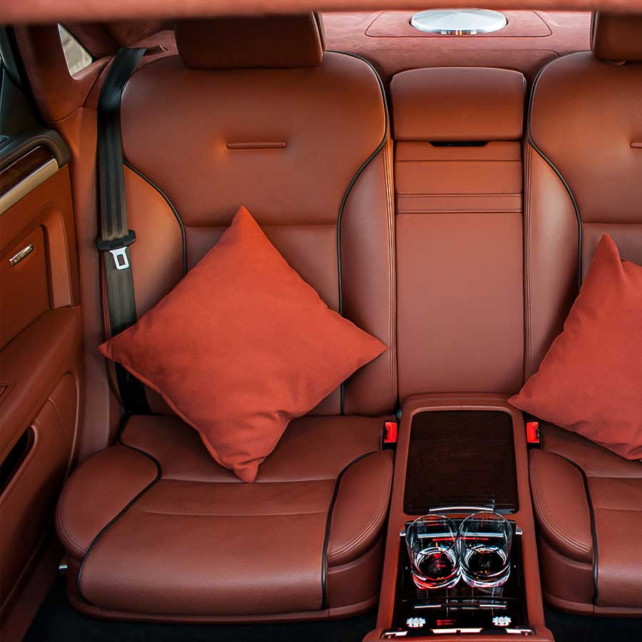 Rücksitze eines Autos in braunem Leder mit zwei Kissen und Mittelkonsole.
