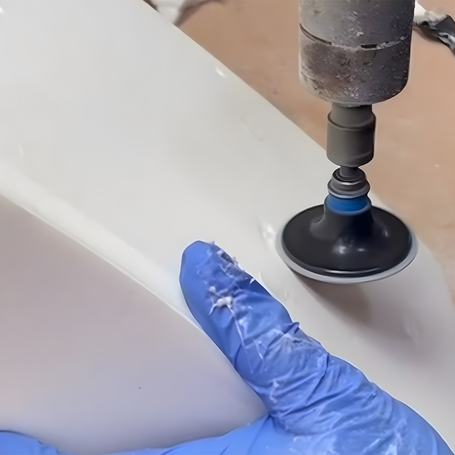 Person mit blauem Handschuh poliert eine weiße Oberfläche mit einem rotierenden Werkzeug.
